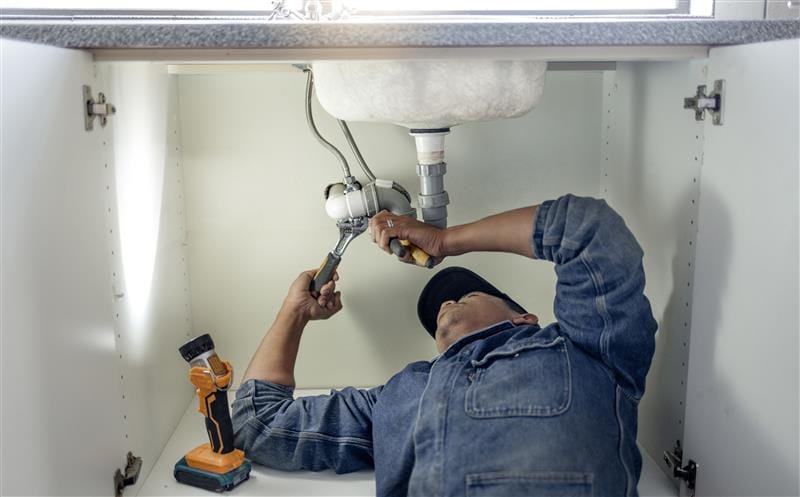 Plumber repairing pipes beneath a bathroom sink in Auburndale