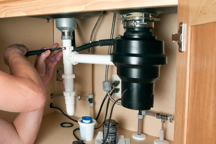 Plumber installing a garbage disposal beneath a kitchen sink in Auburndale