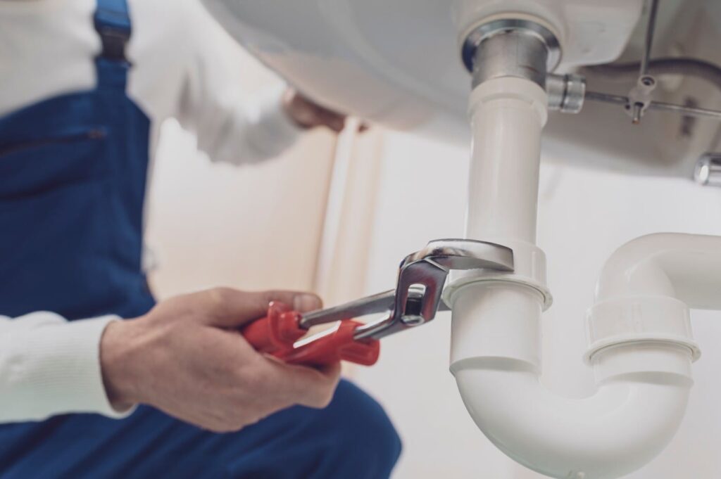 Plumber repairing a white drain pipe beneath a sink in Auburndale